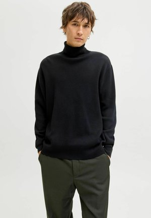 Sort turtleneck sweater med en tekstureret overflade, afslappet pasform og lange ærmer, parret med olivengrønne bukser.