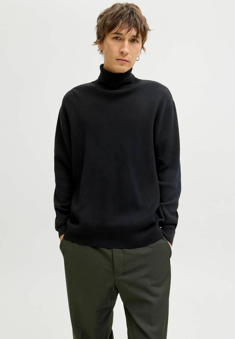 Maglione nero a collo alto con superficie texture, vestibilità relaxed e maniche lunghe, abbinato a pantaloni verde oliva.