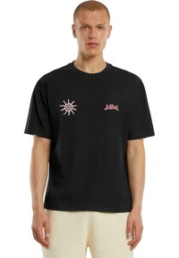 Černé bavlněné tričko s růžovým sluncem a logem značky, kulatý výstřih, krátké rukávy a volný střih. Měkká textura s minimálními designovými prvky.