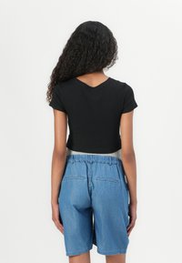 Svart kortermet crop top og lyseblå denimshorts med elastisk liv og baklommer, sett fra baksiden.