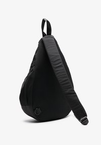 Black sling bag made of textured mesh and smooth fabric. Features a wide adjustable strap and a slim profile with a zip pocket.