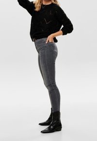 Schwarzer gestrickter Pullover, graue enge Jeans und schwarze Stiefeletten. Strukturierter Pullover mit lockerer Passform; die Jeans haben Standardtaschen und ein elegantes Design.