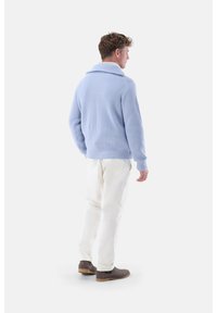 Helles blaues geripptes Sweatshirt mit weitem Kragen, kombiniert mit weißen Hosen und grauen Stiefeletten, von hinten betrachtet.