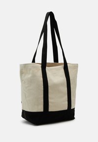 Sac en toile beige avec un fond et des anses noirs. Dispose de deux poignées noires solides et d'une forme rectangulaire simple et spacieuse.