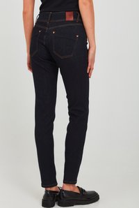 Jeans skinny azul oscuro hechos de mezclilla con costuras naranjas, cinco bolsillos y un parche de cuero en la parte trasera de la cinturilla.
