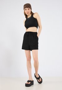 Black ribbed crop top with a high neckline paired with black textured shorts featuring an elastic waistband and pockets. The model wears black platform sandals.