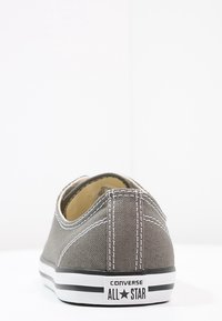 Baskets en toile grise avec coutures blanches, design bas, semelle en caoutchouc et bande noire ; arborent le logo "Converse All Star" sur le talon.