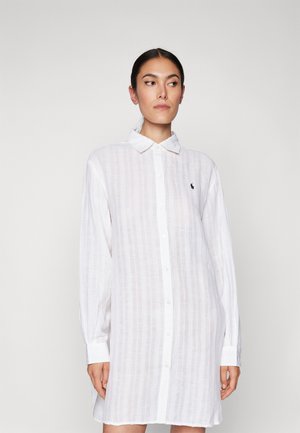 Abito camicia bianco a maniche lunghe realizzato in tessuto leggero a righe, con chiusura a bottoni e un piccolo emblema sul petto.