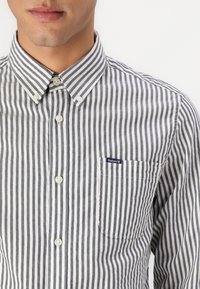 Striped button-up shirt with narrow black and white vertical stripes. Features a classic collar, pocket, and small logo on the chest.