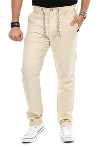 Beige, leichte Baumwollmischung-Hosen mit einem Kordelzugbund, Fronttaschen und einer schlanken Passform, kombiniert mit weißen Sneakern.