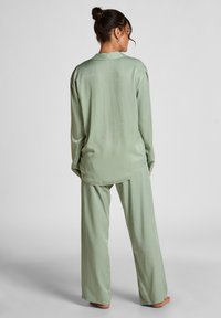 Groene satijnen pyjama set met een langemouwen top met een kraag en losse, recht gesneden broek. Zachte, glanzende textuur met een relaxte pasvorm.