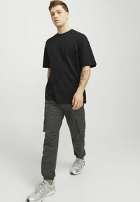 Sort oversized t-shirt, grå cargobukser med lommer og sølvfarvede sneakers. Casual outfit med afslappet pasform og struktureret stof.