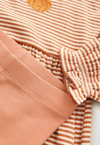 Orange and white striped fabric with a small embroidered bear face, paired with solid orange ribbed fabric.