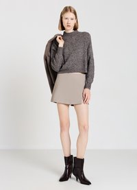 Cropped, dark gray knit sweater paired with a beige mini skirt and black ankle boots with a pointed toe. Smooth texture and fitted design.