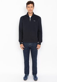 Felpa navy blue a mezza zip con polsini e orlo a coste, abbinata a jeans di denim scuro e sneakers blu. Design semplice e informale.