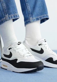 Tenisi albi Nike cu accente negre. Caracteristicile includ un superior din plasă și piele, design cu șireturi și amortizare Air în talpă.