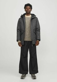 Sort pufferjakke med tekstureret finish, hætte og lynlås-lommer. Brugt over en lys grå strikket sweater og sorte vide bukser, sat sammen med sneakers.