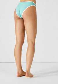 Bas de bikini bleu aqua avec bord blanc, en tissu lisse et extensible, présentant une coupe taille basse. Affiché de dos avec des jambes nues.
