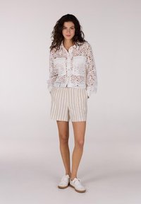 Witte kanten button-up shirt met twee opgestikte zakken, gecombineerd met lichtbeige gestreepte shorts en witte sneakers. Gladde texturen, casual ontwerp.
