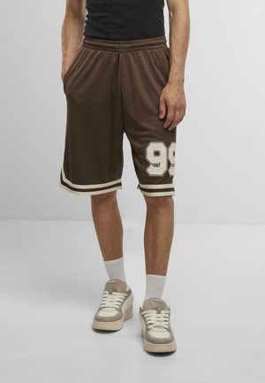 Braune Sportshorts mit weißen Akzenten, versehen mit der Nummer 99, elastischem Bund und Seitentaschen. Kombiniert mit beigen Sneakers und weißen Socken.