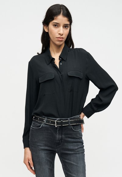 Μαύρο πουκάμισο μακρυμάνικο με γιακά που κουμπώνει, δύο τσέπες στο στήθος, συνδυασμένο με σκούρο γκρι τζιν και μαύρη ζώνη με τρουκς.