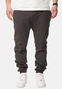 Dunkelgraue Jogginghosen mit elastischen Bündchen und einem lässigen Schnitt, kombiniert mit weißen Sport-Sneakern. Glatte Textur, minimalistisches Design.