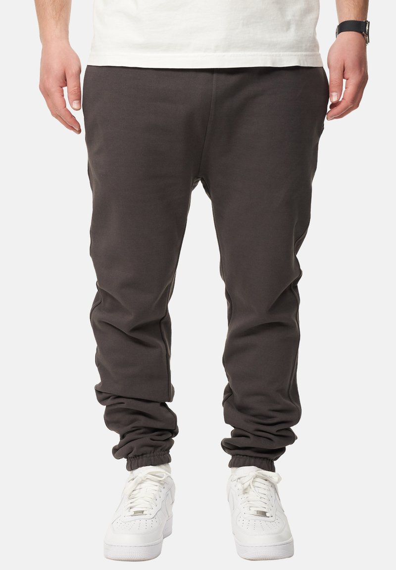 Dunkelgraue Jogginghosen mit elastischen Bündchen und einem lässigen Schnitt, kombiniert mit weißen Sport-Sneakern. Glatte Textur, minimalistisches Design.