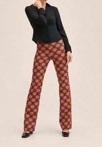 Pantalons évasés avec un motif floral vibrant, comportant des fleurs roses avec des cœurs orange sur un fond noir. Associés à une chemise noire à boutons.