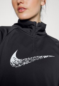 Felpa nera con zip a mezzo collo realizzata in tessuto liscio, caratterizzata da un grande logo Nike swoosh bianco con un design texturizzato.