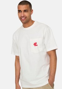 Weißes Baumwoll-T-Shirt mit kurzen Ärmeln, ausgestattet mit einer Brusttasche und rotem Textgrafik auf der Tasche. Weicher Stoff, klassischer Schnitt.