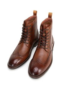 Hnědé kožené kotníkové boty s brogue detaily, hladkým a texturovaným povrchem, šněrovacím designem a poutky na zadní straně.