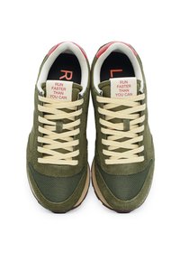 Sneaker in Olivgrün mit einem strukturierten Wildleder- und Mesh-Obermaterial, cremefarbenen Schnürsenkeln und kontrastierendem roten und weißen Text auf der Zunge.