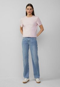 Kurzes, pinkes T-Shirt mit Rundhalsausschnitt, kombiniert mit hellblauen geraden Jeans und weißen Sneakers mit beigen Akzenten.