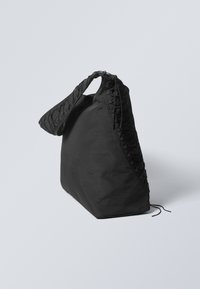 Black fabric shoulder bag with a textured, braided strap. The bag has a triangular shape and a minimalistic design, featuring a cinched closure.