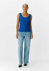 Top sin mangas de rayas azul con escote en u, combinado con jeans rectos azul claro y tacones de punta negros. Diseño y ajuste minimalista.