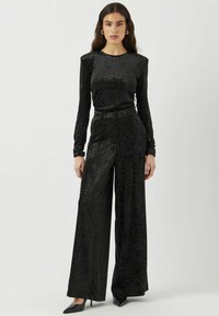 Mono negro de manga larga, hecho de una tela suave con un estampado de lunares blancos. Diseño de pierna amplia, cintura ajustada y ligero brillo.