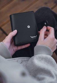 Black leather wallet with a snap closure, featuring silver hardware and embossed logo. Compact design, smooth texture, and minimalist aesthetic.