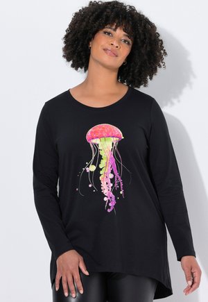 Femme aux cheveux bouclés portant un t-shirt noir à manches longues avec un graphique coloré de méduse rose et verte.