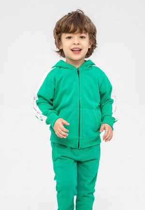 Veste à capuche verte zippée avec poches kangourou, associée à un pantalon assorti. Présente des accents blancs sur les manches, fabriquée dans un matériau doux et extensible.