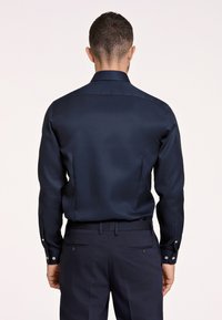 Camisa de manga larga azul marino hecha de tejido suave, con cuello clásico y puños abotonados, acompañada de pantalones oscuros ajustados.