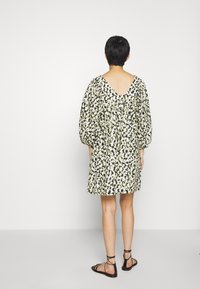 Šaty s květinovým vzorem v světle zelené a černé barvě, volného střihu, s V výstřihem vzadu a vypuštěnými rukávy. Doplněné o černé sandály na pásku.