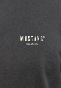 Szürke pamut pulóver, amelynek elején fehér betűkkel szerepel a "MUSTANG CLASSICS" felirat. A textura sima, egyenletes kötött mintázattal.