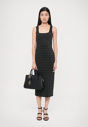 Rochie neagră tricotată, cu decolteu pătrat și model cu logo MK pe întreaga suprafață. Asortată cu o geantă neagră decorată cu talismane și lanț auriu.