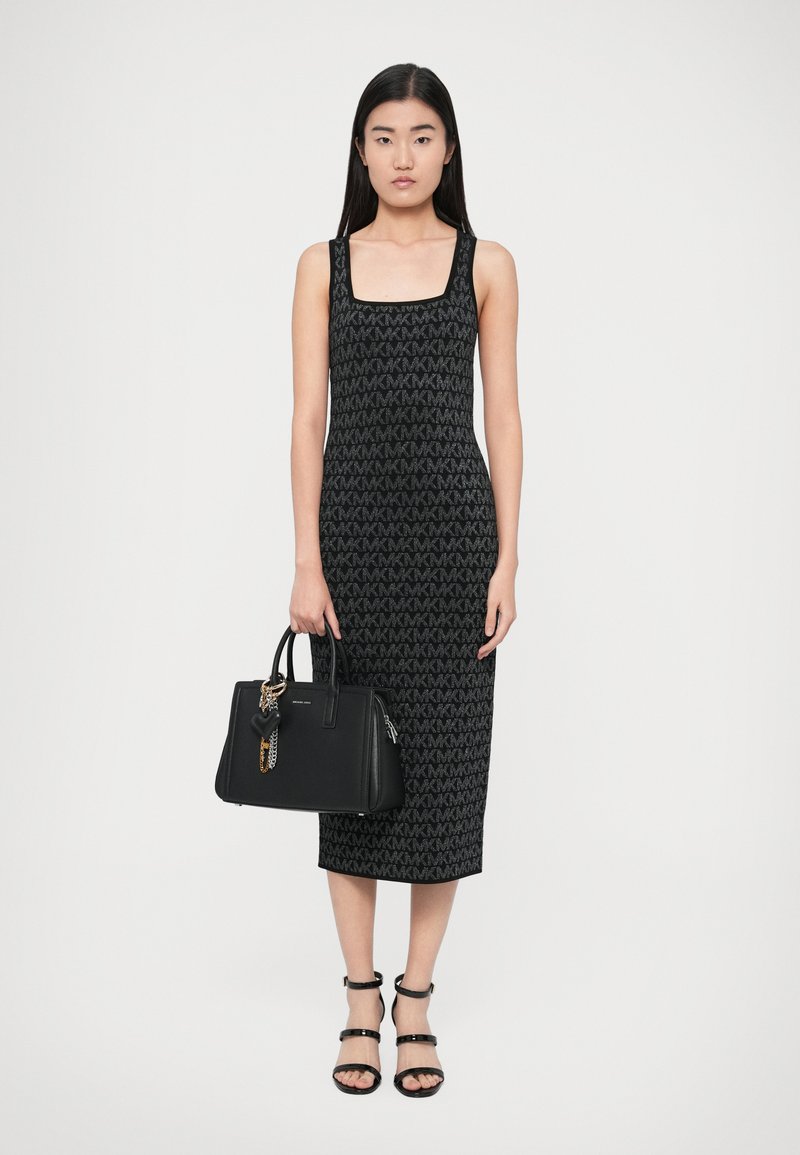 Μαύρο πλεκτό φόρεμα με τετράγω νη λαιμόκοψη και μοτίβο με λογότυπο MK σε όλο το ύφασμα. Συνδυάζεται με μαύρη τσάντα χειρός διακοσμημένη με γούρια και χρυσή αλυσίδα.