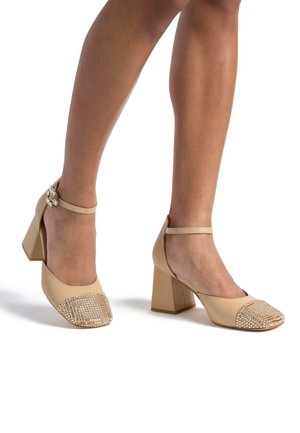 Chaussures à talons block beiges avec une tige en cuir lisse et un embout décoré de strass étincelants, dotées d'une bride à la cheville.