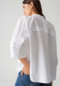 Witte, oversized blouse met een ronde zoom, verlaagde schouders en opgerolde mouwen; lichte stof met een gladde textuur en een minimalistisch ontwerp.