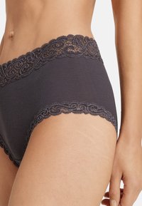 Svart bomullsboxer med intrikata spetskanter längs midjan, som visar en slät textur och en klassisk hipsterdesign.