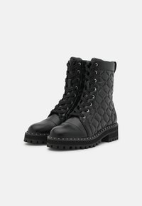 Botas de tobillo negras con cordones que presentan un diseño de cuero acolchado, punta redondeada y una suela de goma gruesa con tachuelas en tono plateado a lo largo del borde.