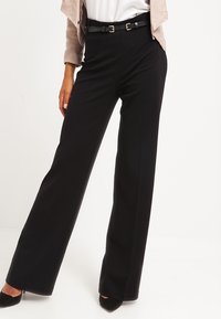 Zwarte wijde broek van zachte stof, met een tailleband en een getailleerde pasvorm, aangevuld met subtiele naden en een uitlopende stijl.
