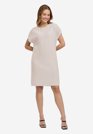 Strickkleid in hellbeige, kurze Ärmel, lockere Silhouette, strukturmuster, knielang, kombiniert mit schwarzen Riemchensandalen.